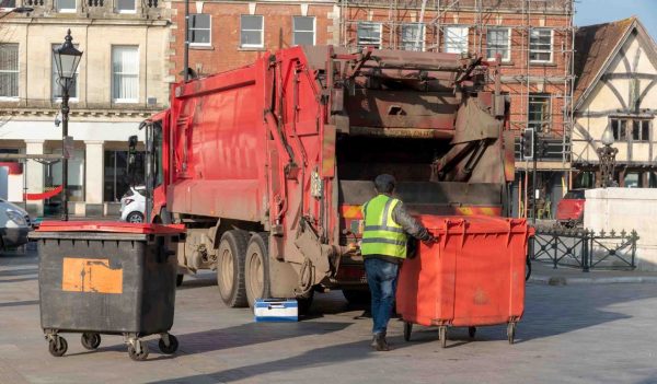 Operative loading a commercial size black refuse bin into a truck