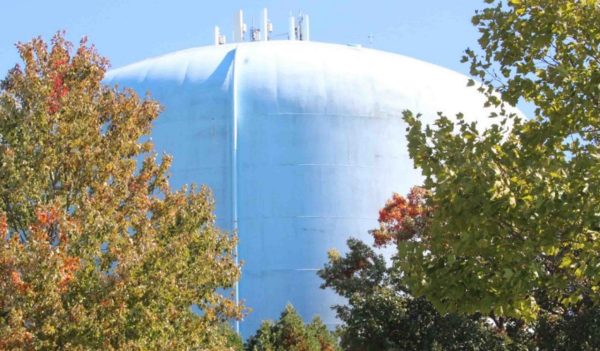 Close up of a white water storage tank showing between two trees.