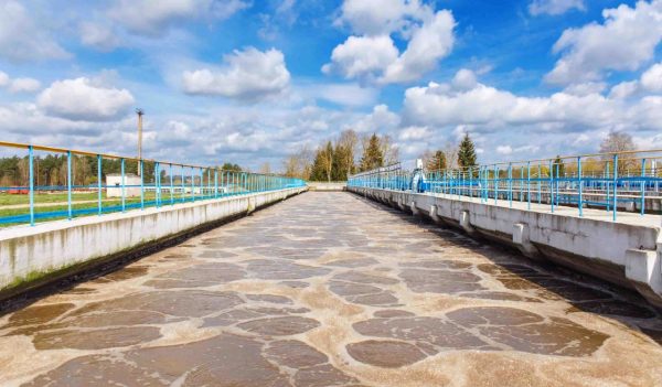 Sewage treatment plant aeration tanks with trees and a blue sky with clouds in the background.