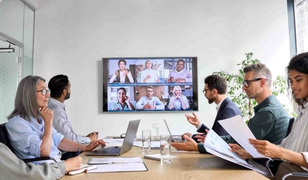 Diverse company employees having online business conference video call on tv screen monitor in board meeting room. Videoconference presentation, global virtual group corporate training concept.