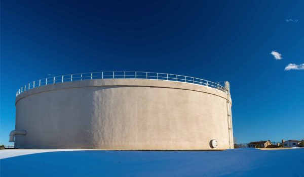 Large municipal concrete water storage tank with the blue sky in the background and snow on the ground.