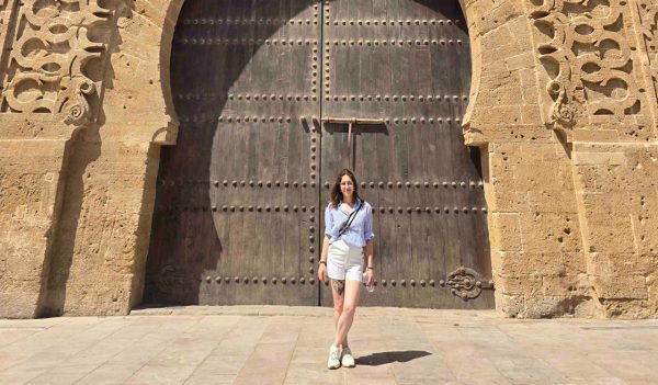 Beatriz Maria Lima Mendes standing in front of large historical iron doors.