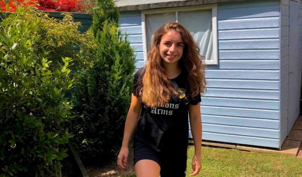 Charlie Anne Briggs outside in front of a blue backyard shed.