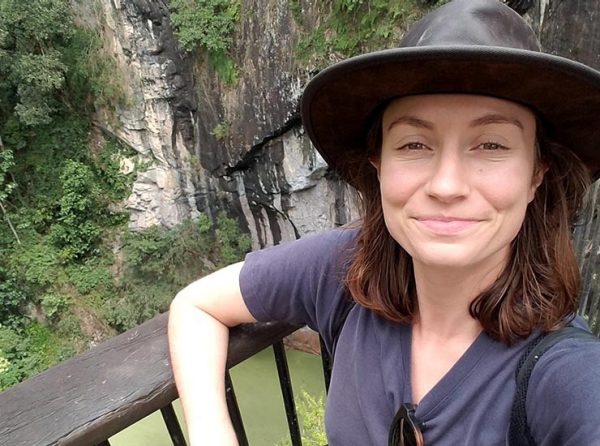 Marelle Davey standing against a railing looking over a river with a rock cliff in the background.