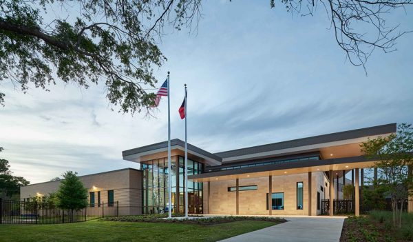 Exterior of the school with a walkway to the main entrance, plantings, and flags flying