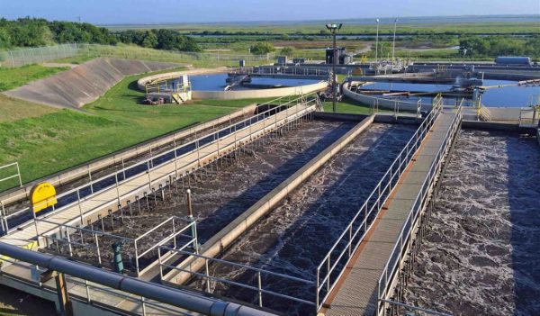 Aerial view of waste water treatment plant digester and storage tanks, surrounded by green fields.